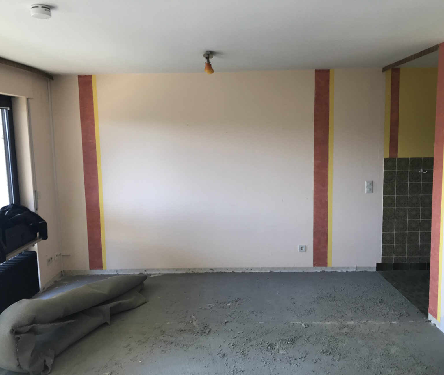 Innenraum einer Wohnung im Rohbau-Zustand vor der Sanierung und nach dem Ablauf einer Entrümpelung mit unverputzten Wänden, Estrichboden und sichtbaren Elektroinstallationen.