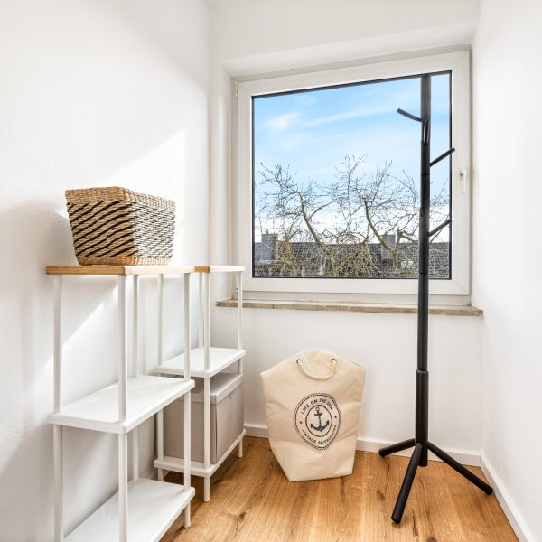 Moderner schwarzer Garderobenständer in Baumform aus Massivholz in einem hellen, minimalistisch eingerichteten Raum.